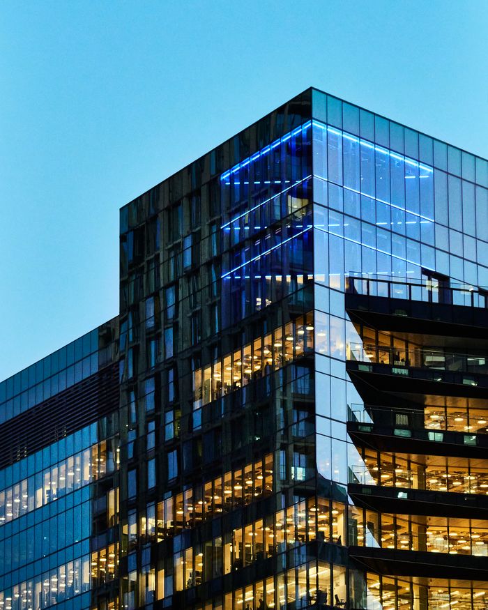 A sleek glass office building with illuminated interior visible against a twilight sky.